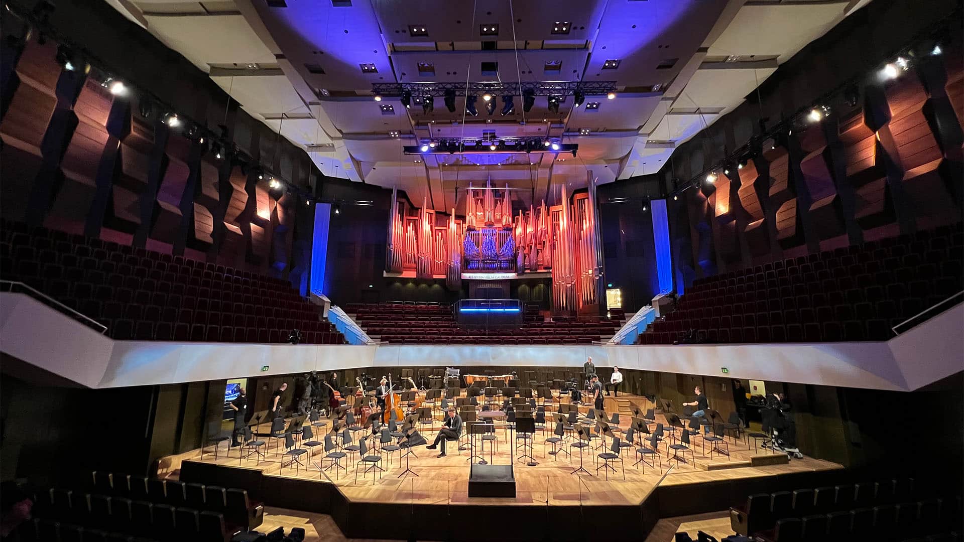 Concert hall interior with an orchestra setup, featuring a large organ and tiered seating.